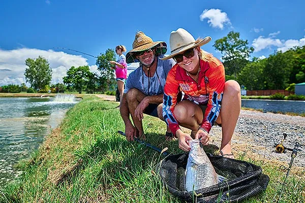 Smiling guests landing a barramundi at the Hook-A-Barra ponds