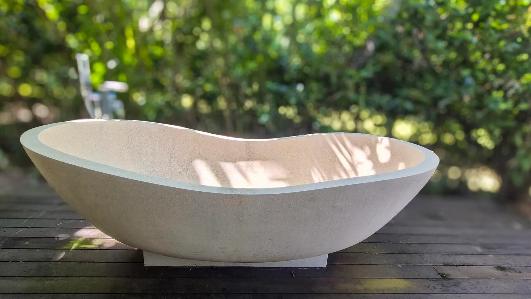 Stone outdoor bath on a timber deck under the palms